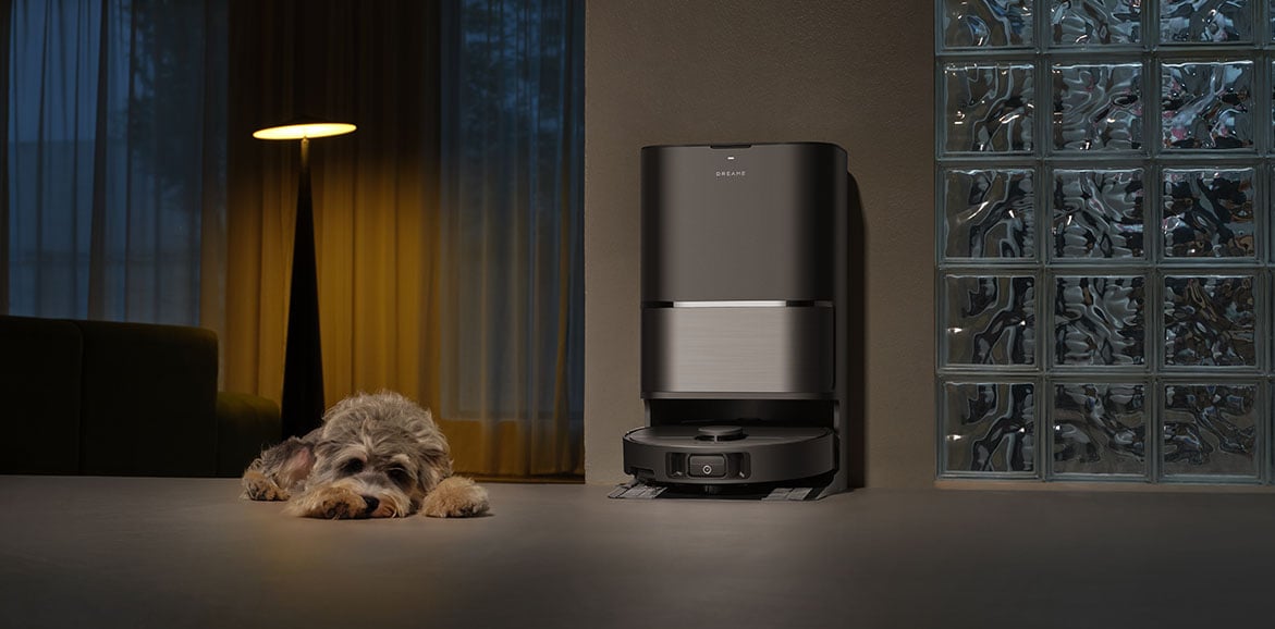 Czarna stacja dokująca z robotem sprzątającym Dreame w ciemnym pomieszczeniu obok leżącego psa